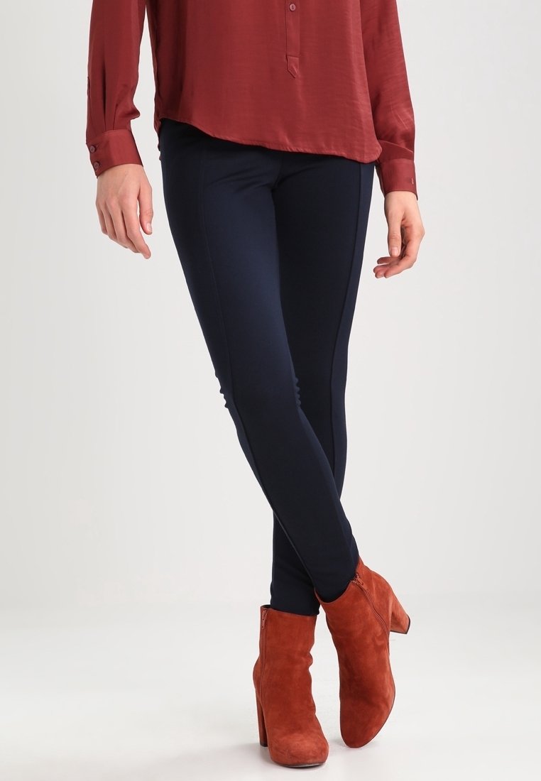 Marinblå snäva byxor i elastiskt tyg, i kombination med rustfärgade mocka ankle boots. Skjortan är mörkröd och har en knapp-up-design.