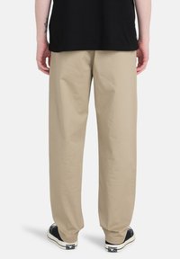 Beige bomuldsbukser med en afslappet pasform, der har en glat overflade. Parret med sorte sneakers, der viser hvide detaljer.