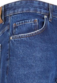Jeans de denim azul, con un corte clásico, costuras visibles, un pequeño bolsillo trasero y una etiqueta de cuero marrón en la cintura.