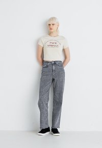 Vaqueros grises con adornos de piedra en el dobladillo, de cintura alta, combinados con una camiseta cropped crema con estampado rojo y zapatillas negras.
