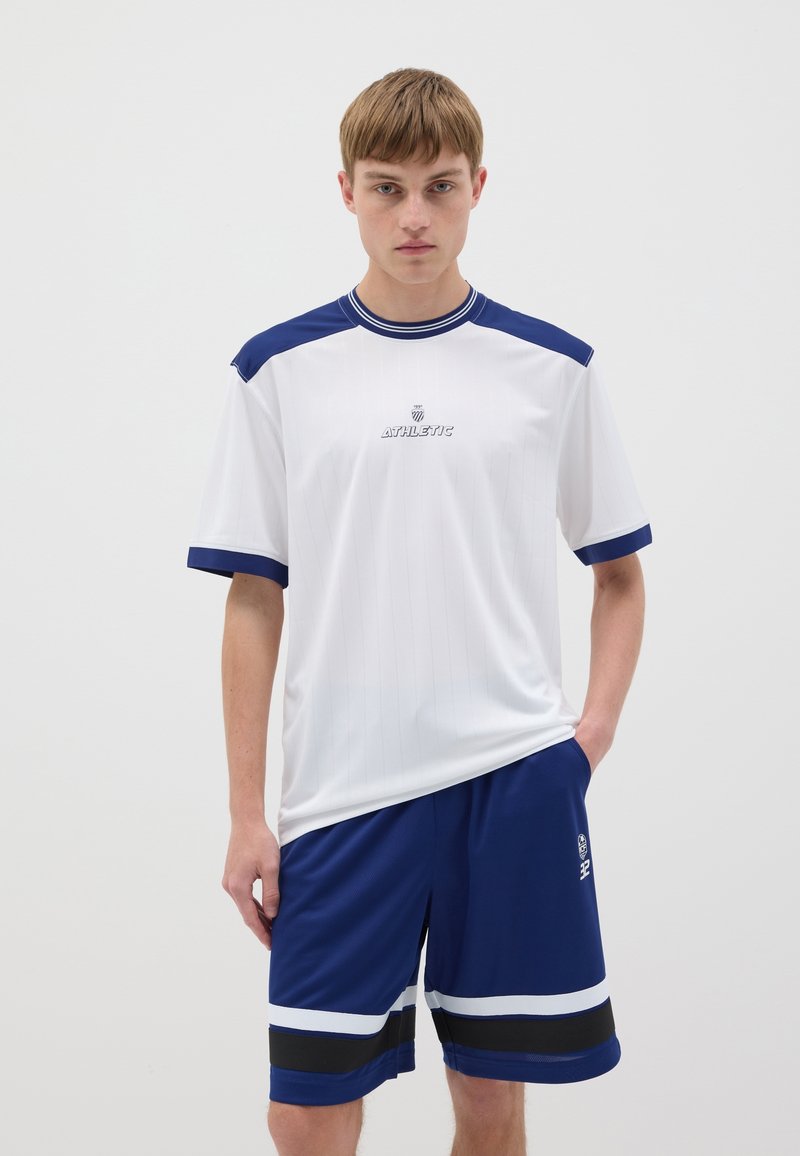 Ensemble de vêtements de sport athlétiques comprenant un t-shirt blanc à manches courtes avec des accents bleus et un short bleu assorti avec des détails en rayures horizontales.
