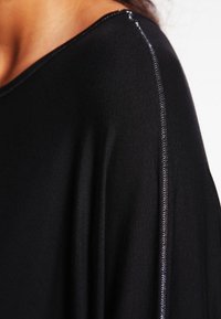 Top nero con una vestibilità ampia, caratterizzato da un accento argentato lucido lungo la cucitura della spalla e una texture morbida e liscia.