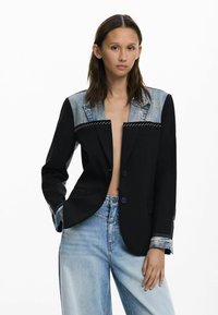 Čierny blazer s denimovými akcentmi, klopovými l�ímci, kontrastným prešívaním a dvoma prednými vreckami. Voľné džínsy zo svetlomodrého denimu.
