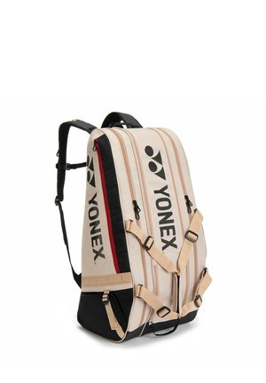 Zaino sportivo Yonex beige e nero con più scomparti con cerniera, spallacci regolabili e logo marchiato sulla parte anteriore e sul lato.