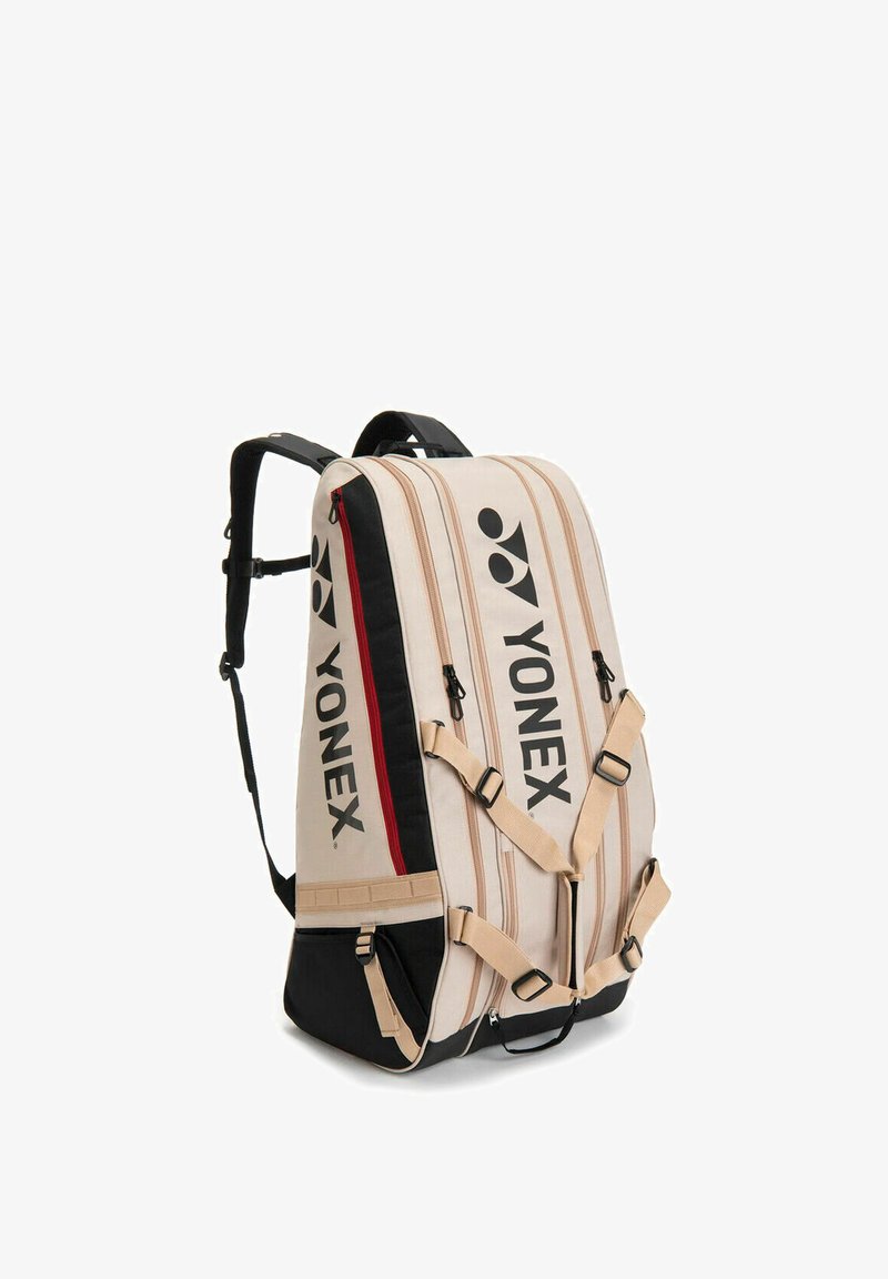 Beige en zwarte Yonex sportrugzak met meerdere ritsvakken, verstelbare schouderbanden en merklogo op de voorkant en zijkant.