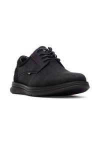 Zapato de ante negro con puntera redondeada, acento marrón en contraste, diseño de cordones y suela de goma flexible. Detalle de hardware minimalista.