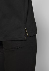 Black T-shirt featuring a side split with yellow stitching detail, made of soft cotton fabric with a smooth texture, paired with black pants.