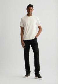 Weißes T-Shirt mit kurzen Ärmeln und Rundhalsausschnitt, kombiniert mit schwarzen Jeans und schwarzen Sneakers, aus einem glatten Stoff.
