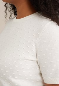 Biały dziergany sweter z krótkim rękawem, ozdobiony fakturowanym wzorem z małych wypukłych kropek oraz ściągaczowym dekoltem i mankietami rękawów.