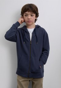 Hanorac bleumarin cu fermoar frontal, glugă cu șnur și buzunare tip cangur. Material din amestec de bumbac, manșete și tiv din reiat.