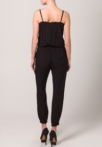 Combinaison noire avec fines bretelles, coupe ample, taille élastique et jambes fuselées. Caractérisée par un tissu lisse et sans accents supplémentaires.