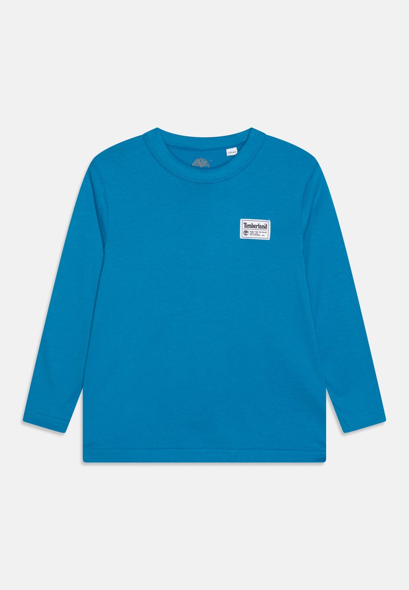 Long-sleeve shirt in bright blue cotton, featuring a round neck and a small white Timberland logo patch on the left chest. Smooth texture.