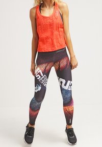 Top senza maniche rosso con motivo testurizzato; leggings neri aderenti con stampa a serpente colorata e loghi; scarpe da atletica nere.