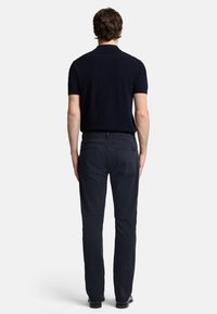 Polo shirt blu navy a maniche corte abbinato a pantaloni blu scuro, con design a gamba dritta e tessuto texturizzato, visto da dietro.
