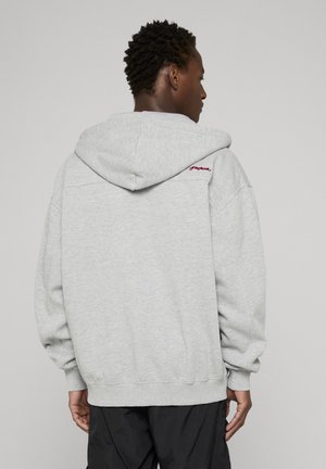 Sweat à capuche gris avec une finition texturée, doté d'une capuche à cordon, de poignets côtelés et d'un logo brodé sur l'épaule.