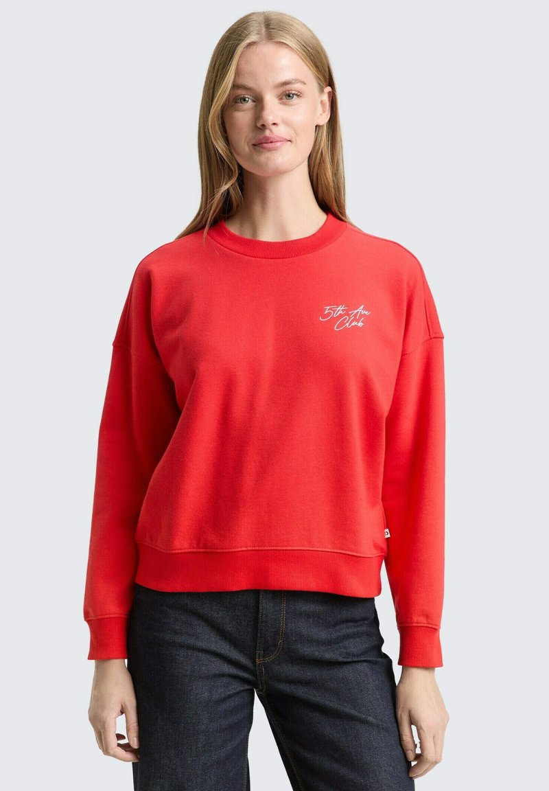 Rode sweatshirt met een ronde hals, doorgezakte schouders en een wit geborduurd logo. Zachte textuur met een ontspannen pasvorm en geribbelde manchetten.