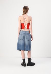 Top corto rojo con tirantes blancos, con un respaldo entrecruzado, combinado con pantalones cortos de mezclilla azules hasta la rodilla y botas negras gruesas.