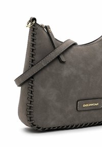 Gray faux suede handbag with a curved shape, featuring stitched detailing, a gold brand plaque, and a shoulder strap.