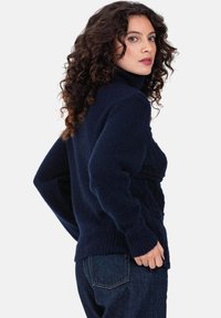 Pull à col roulé bleu marine avec motif en maille texturée et poignets côtelés. Porté avec un jean foncé, il présente une coupe décontractée et un tissu doux.