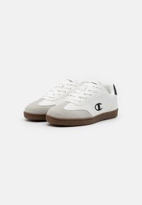 White sneakers with grey suede accents, rubber sole, lace closure, and logo on the side. Smooth leather finish with rounded shape.