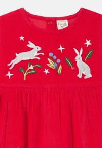 Rochie roșie din corduroy cu iepurași gri brodați, crenguțe de iederă și boabe. Dispune de un decolteu rotund și o fustă plisată. Material din bumbac organic.