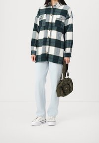 Zielono-biała flanelowa koszula w kratę, zapinana na guziki, z dwoma kieszeniami na piersi; jasnoniebieskie dżinsy; oliwkowozielona torba na ramię; białe trampki.