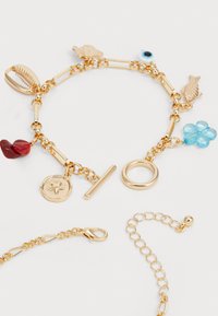 Gouden armband met textuurbedeltjes, waaronder schelpen, vissen en een blauwe bloem, met een sluiting met draaiknop en een schakelkettingontwerp.