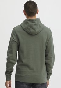 Green hooded sweatshirt featuring a textured fabric, long sleeves, and a relaxed fit. The back shows a seamless design without patterns.