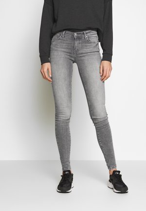 Jeans ajustados en denim gris deslavado, con diseño clásico de cinco bolsillos, pasadores para cinturón y un corte slim, combinados con zapatillas deportivas negras.