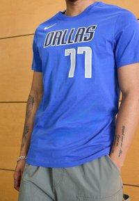 Modrý krátký rukáv dres s nápisem "DALLAS" tučným černým písmem a "77" v bílé barvě, vyrobený z měkkého materiálu s kulatým výstřihem.