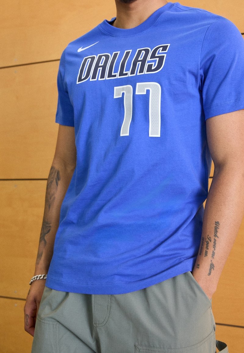 Modrý krátký rukáv dres s nápisem "DALLAS" tučným černým písmem a "77" v bílé barvě, vyrobený z měkkého materiálu s kulatým výstřihem.