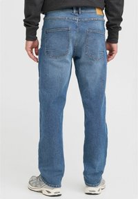 Jeanși din denim albastru cu croială dreaptă, având talie medie, două buzunare spate și o etichetă din piele maro la talie.