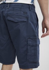 Șorturi cargo bleumarin dintr-un material ușor, cu multiple buzunare, cusături vizibile și un design relaxat.
