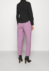 Zwarte langwijdige shirt gecombineerd met lichtpaarse op maat gemaakte broek, met details zoals achterzakken en elegante zwarte hoge enkellaarzen.