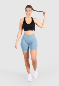 Zwarte geribbelde sportbeha en lichtblauwe high-waisted fietsshorts. De outfit heeft een aansluitend ontwerp en is gecombineerd met witte sportschoenen.