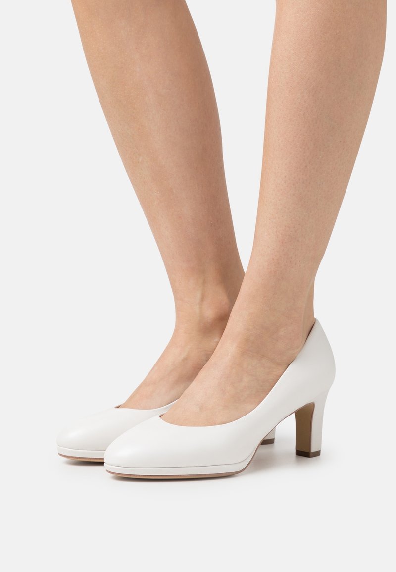 Chaussures à talons hauts blanches avec une texture lisse et brillante et un design à bout arrondi. Elles présentent un talon modeste et des accents de couleur subtils à la base.