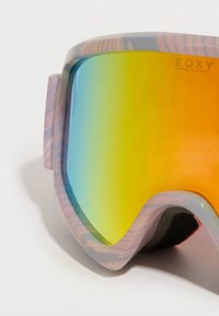 Gogle narciarskie Roxy z kolorową soczewką o gradiencie od niebieskiego do pomarańczowego. Oprawka ma fakturowany różowo-szary wzór z czarną piankową wyściółką.