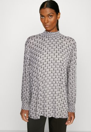 Blouse à manches longues en noir et blanc avec une texture en motif de coquillage, col montant, poignets froncés et tissu léger.