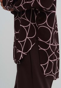 Dark brown blouse with light pink circular pattern, long sleeves, side splits, and a smooth texture, designed for relaxed fit.