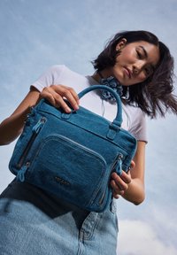 Borsa in denim blu con doppi manici, superficie strutturata, due tasche anteriori con zip e logo del brand cucito sul davanti.