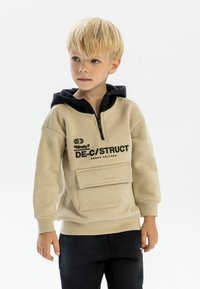 Beige zip-neck hoodie with a black hood, featuring a front pocket, printed text design, ribbed cuffs, and a relaxed fit.