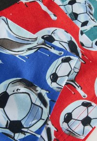 Gros plan sur un tissu imprimé de ballons de football et de trophées argentés brillants sur des fonds rouge et bleu.