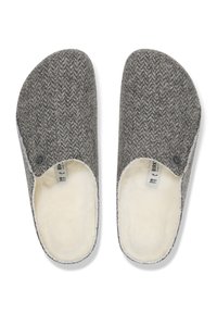 Grå ulltofflor med ett fiskbensmönster, vit konstpälsfoder, sk slip-on-design och en cirkulär logotypdetalj på sidan.