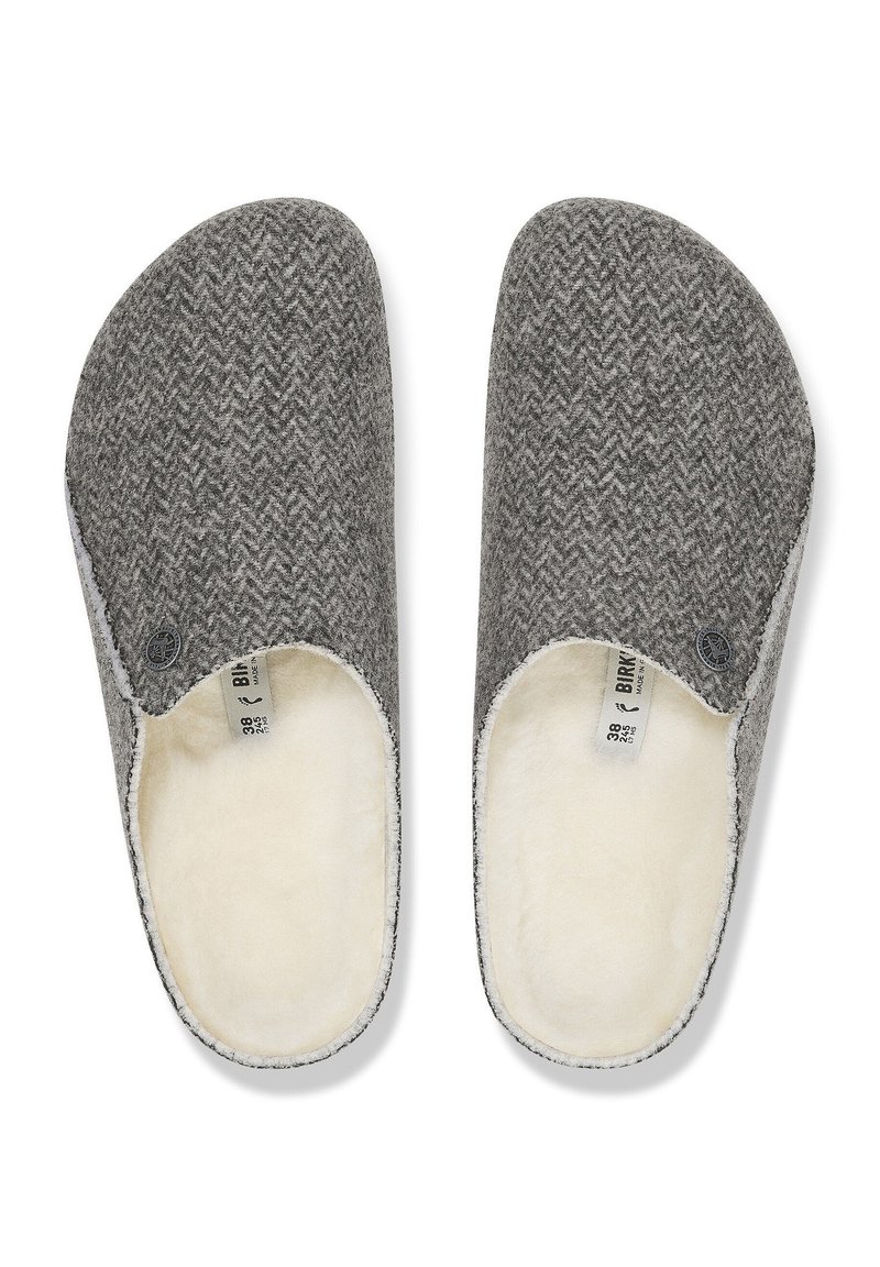 Chaussons en laine gris avec un motif en chevrons, doublure en fausse fourrure blanche, design à enfiler et accent du logo circulaire sur le côté.