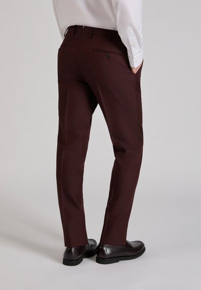 Pantalones personalizados color burdeos con una textura suave, que presentan bolsillos traseros y un ajuste elegante. Combinados con zapatos negros para un look pulido.