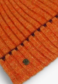 Tela de lana naranja con canalé vertical y un acabado texturizado. Presenta un botón de bronce con un diseño de calavera como un acento notable.