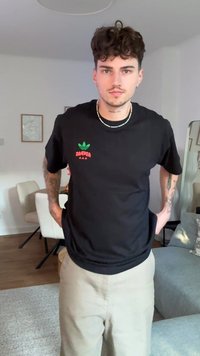 Melna kokvilnas T-krekls ar zaļu un sarkanu grafisku logo kreisajā krūtī. Īsas piedurknes, apaļa kakla izgriezums un brīvs piegriezums.