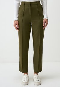 Olive green tailored pants with a high waist, featuring front pleats, tapered legs, and paired with white sneakers. Smooth fabric texture.