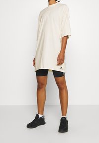 Camiseta oversized beige de tejido suave, con mangas cortas y escote redondeado, combinada con pantalones cortos deportivos negros y zapatillas negras.
