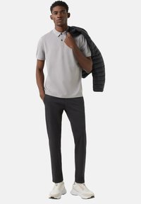 Gray polo shirt with short sleeves, black puffer jacket draped over shoulder, black slim-fit pants, and white sneakers with gray details.